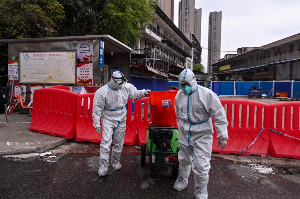 Workers wearing protective suit walk next to Huanan Seafood Wholesale Market in Wuhan, in China's central Hubei province on March 30, 2020, after travel restrictions into the city were eased following more than two months of lockdown due to the COVID-19 coronavirus outbreak. - Wuhan, the central Chinese city where the coronavirus first emerged last year, partly reopened on March 28 after more than two months of near total isolation for its population of 11 million. (Photo by Hector RETAMAL / AFP)